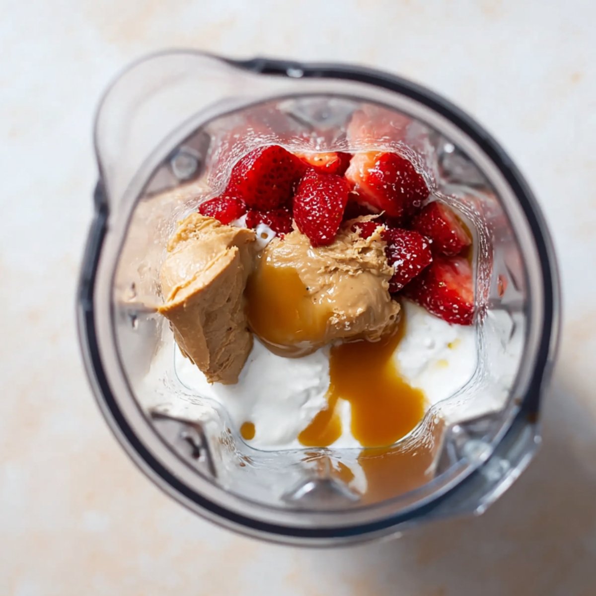 Place the frozen strawberries, Greek yogurt, almond butter, honey, vanilla extract, and almond milk into a high-powered blender.