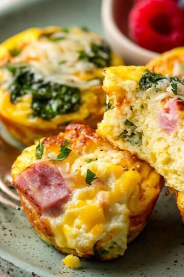 Breakfast Egg Muffins with ham, spinach, and melted cheese, showing the soft, fluffy interior, served with fresh berries.
