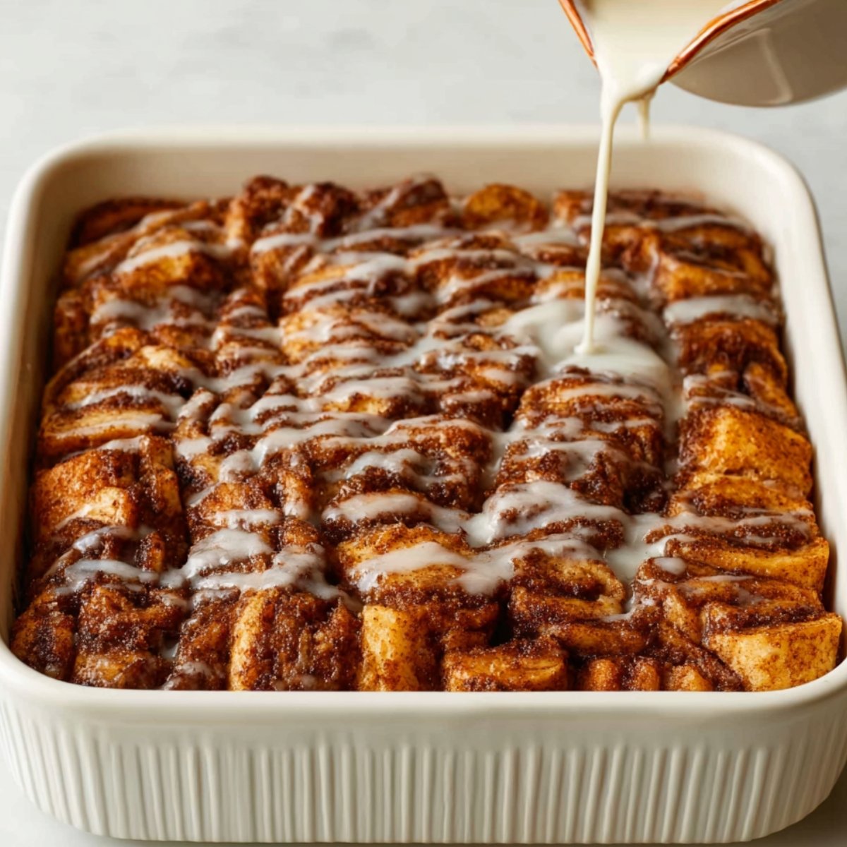 Close-up of a cinnamon roll French toast casserole being drizzled with glaze.