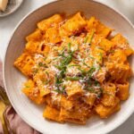 Gochujang Pasta in a creamy orange sauce, topped with grated cheese and fresh green chives, served in a bowl.