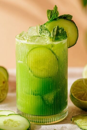 Homemade Cucumber Lime Agua Fresca in a glass, garnished with cucumber slices and mint leaves, with lime wedges and cucumber slices in the background.