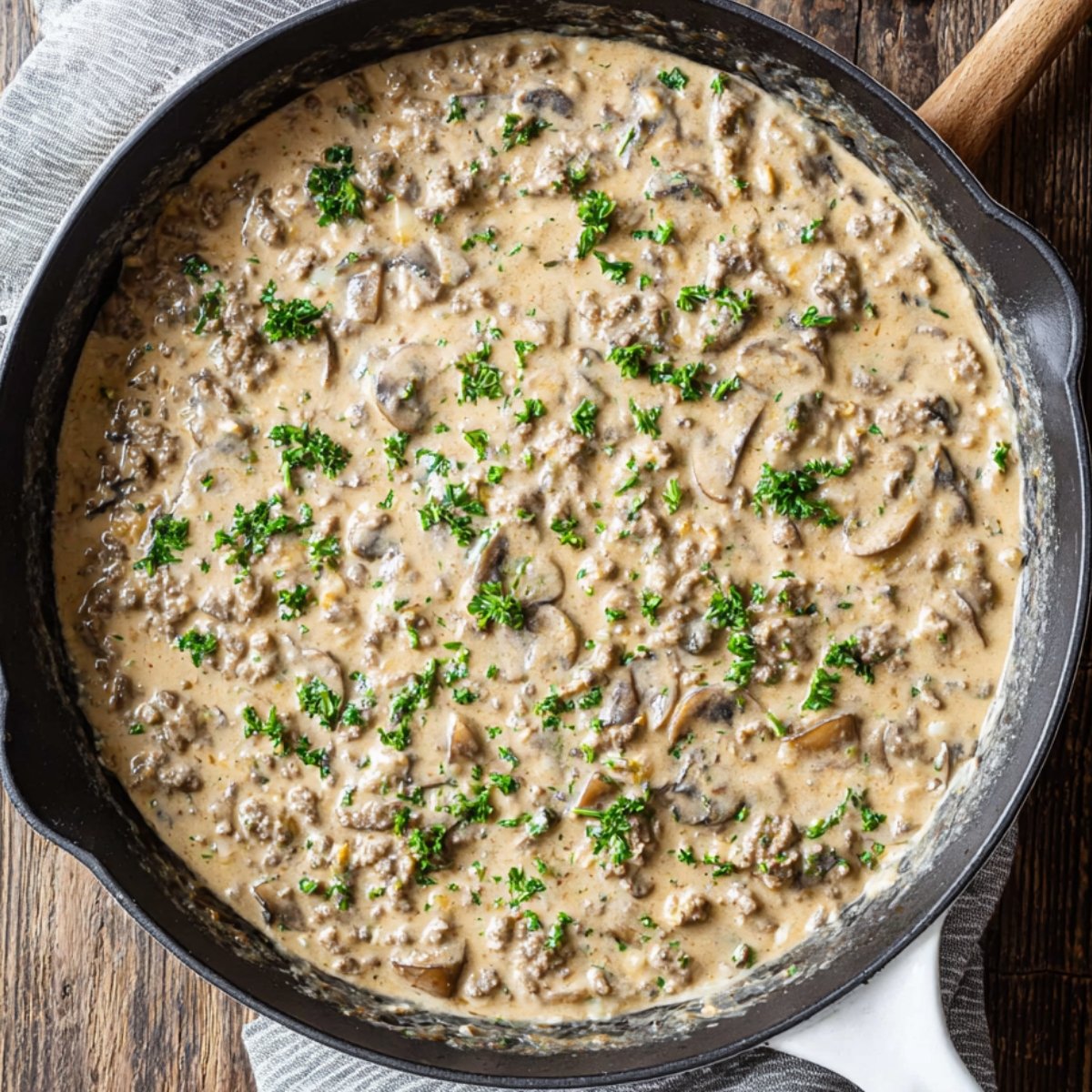 Creamy homemade ground beef stroganoff simmering in a black skillet, filled with tender beef, mushrooms, and fresh parsley on top.