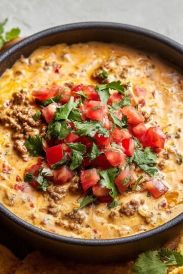 Homemade Rotel Dip topped with fresh diced tomatoes and cilantro, served with tortilla chips on the side.