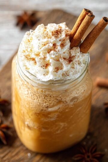 Iced Pumpkin Spice Latte in a mason jar, topped with whipped cream, cinnamon, and two cinnamon sticks.