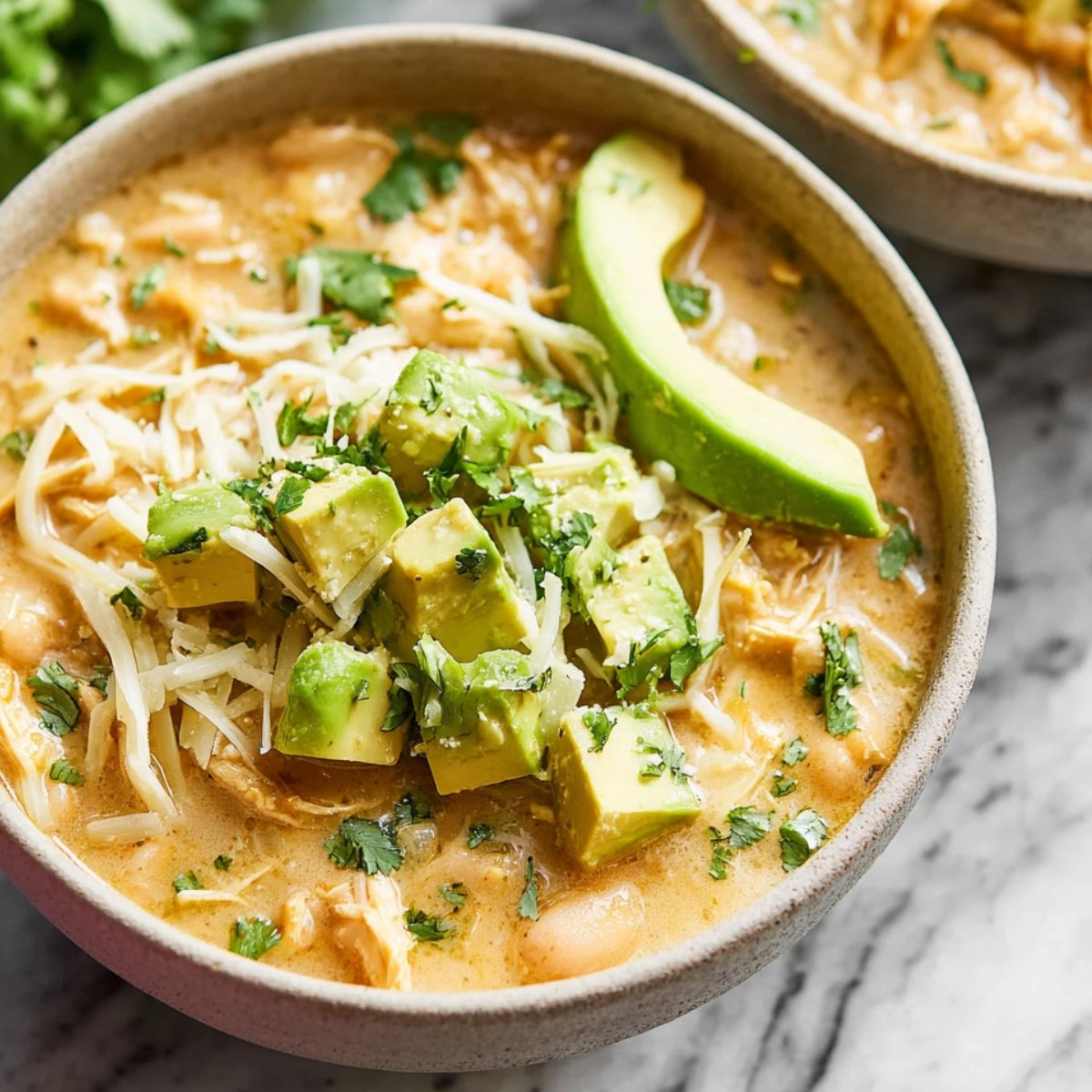White Chicken Chili topped with avocado, shredded cheese, and fresh cilantro.
