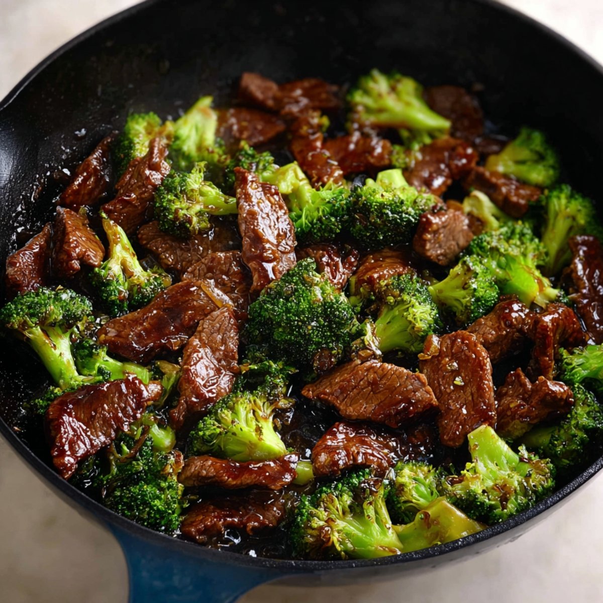 Beef and broccoli stir-fry in a black skillet, coated in savory sauce.