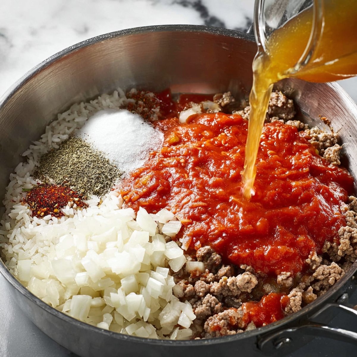 Tomato sauce, rice, spices, and broth added to a pan with cooked meat and onions.