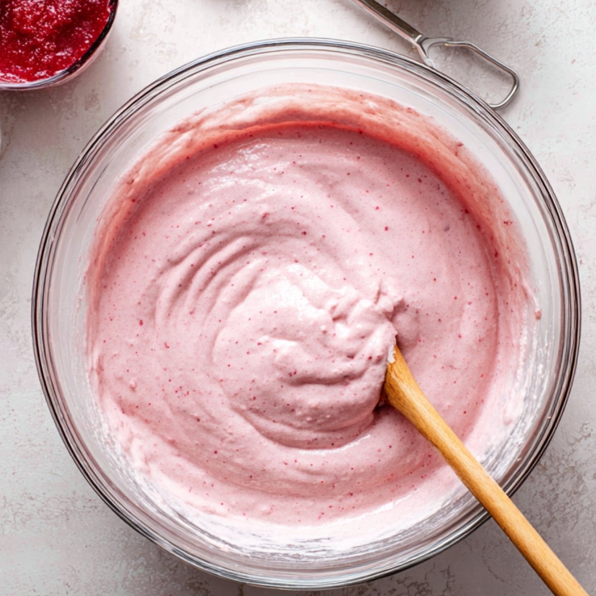 A bowl of strawberry cake batter being stirred with a wooden spoon.