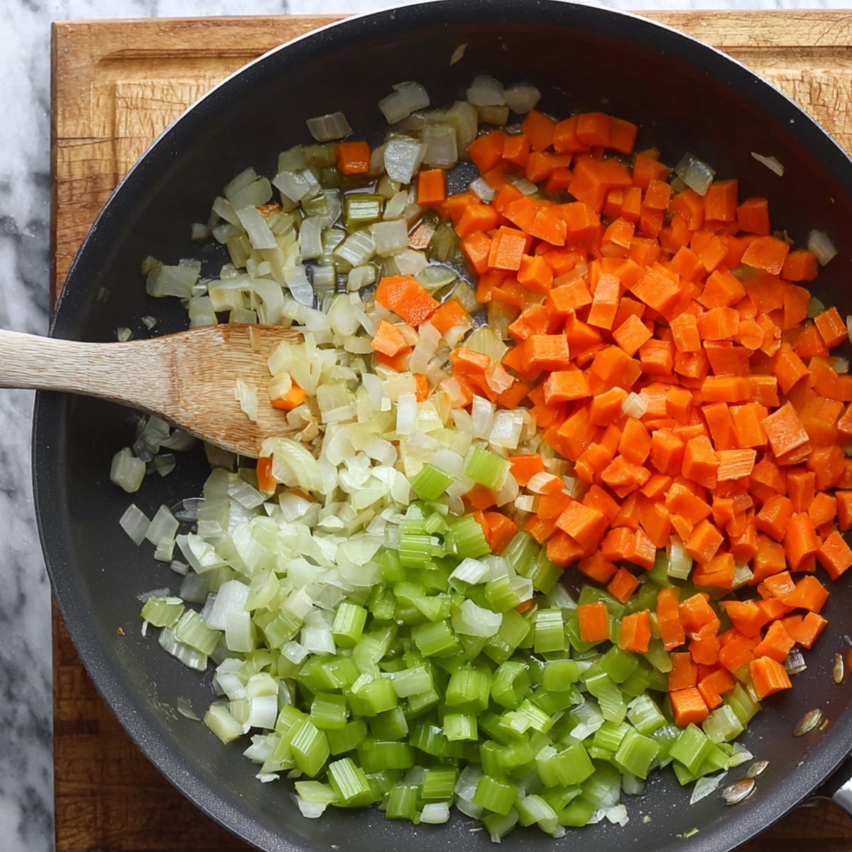 A skillet with diced onions, carrots, and celery being sautéed until tender.