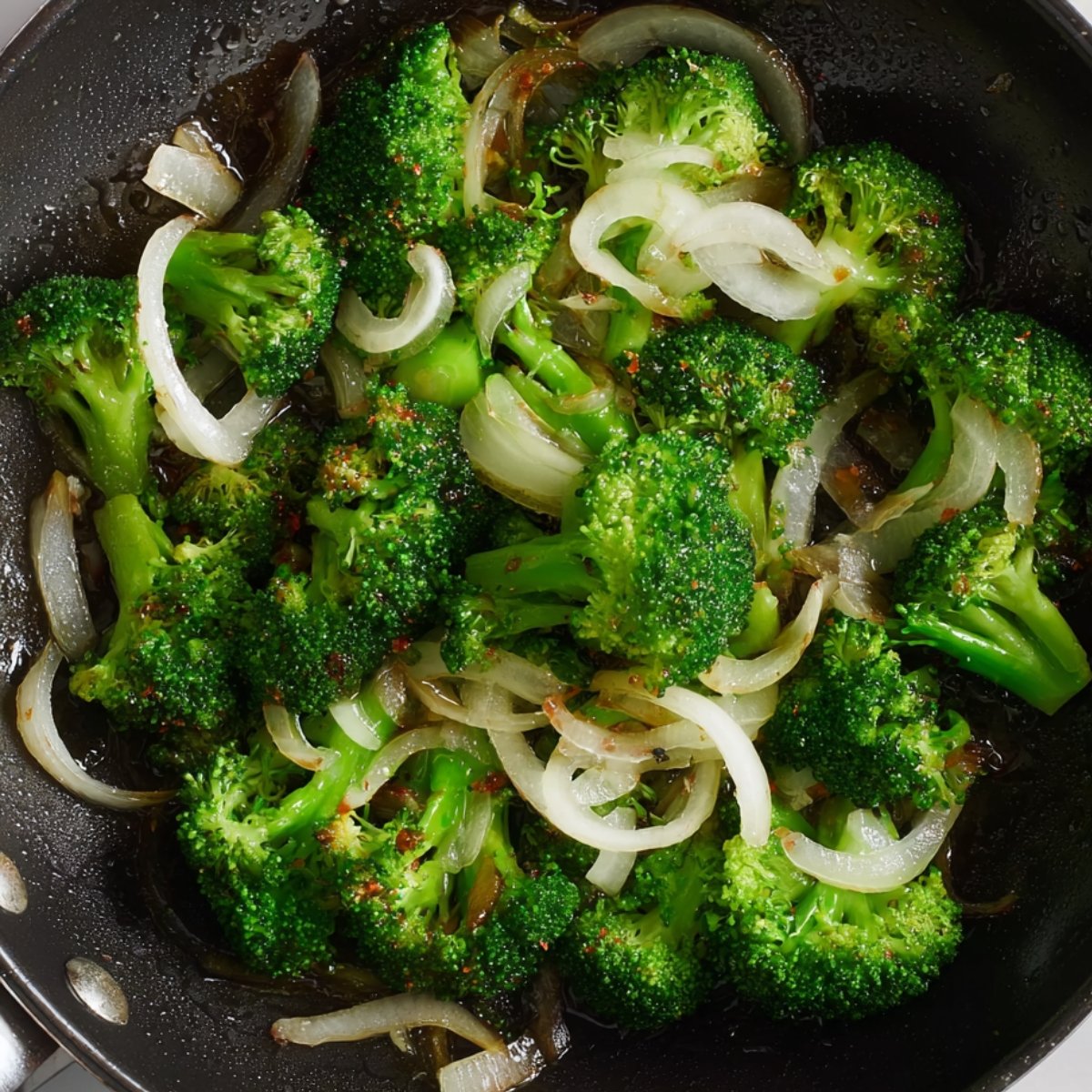 Broccoli and onions sautéing in a pan with seasoning.