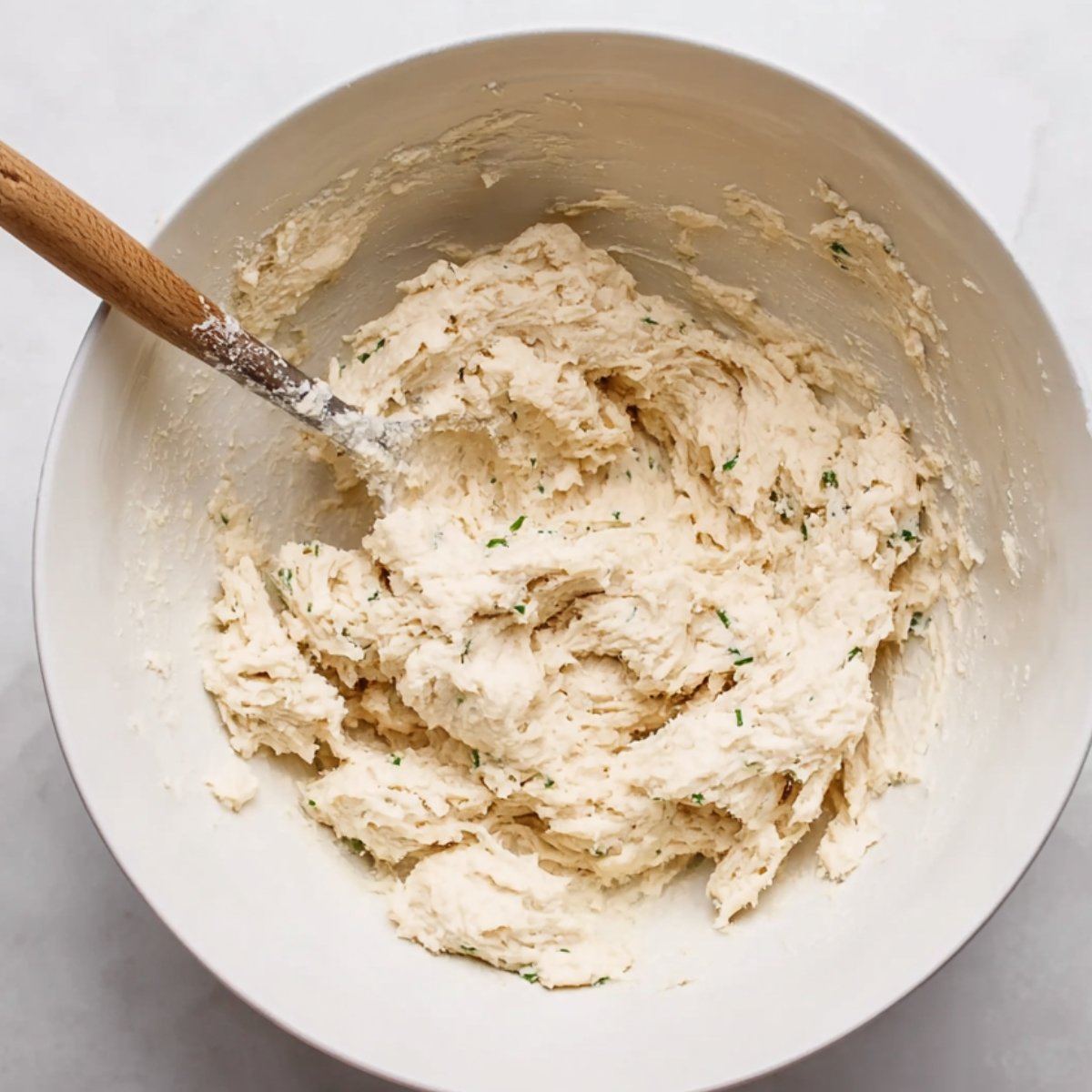 A white bowl filled with dumpling batter, freshly mixed with herbs.