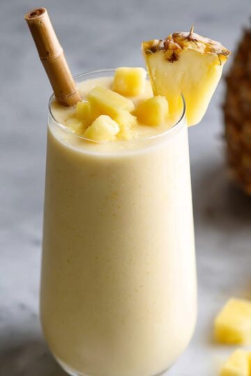 A glass of Pineapple Smoothie topped with pineapple pieces and a bamboo straw.