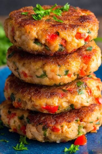Golden-brown, crispy Salmon Patties stacked neatly on a plate, garnished with fresh parsley, ready to be served as a delicious meal.