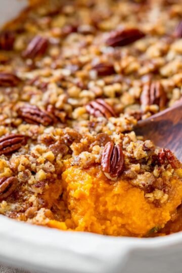 A close-up of a sweet potato casserole with a crisp pecan crumble topping, showing the rich orange sweet potatoes underneath.