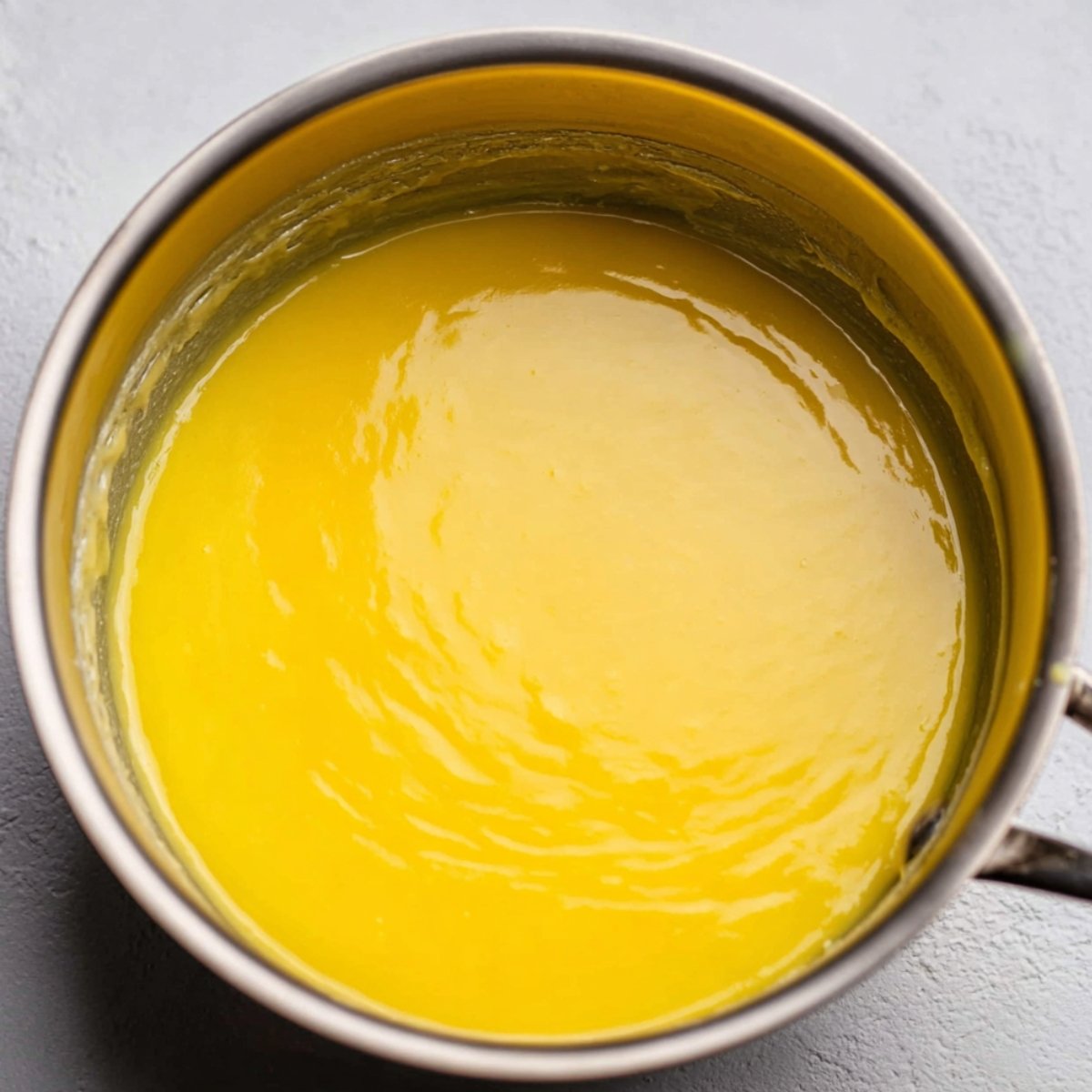 A close-up view of creamy yellow lemon filling in a saucepan, freshly prepared and smooth.